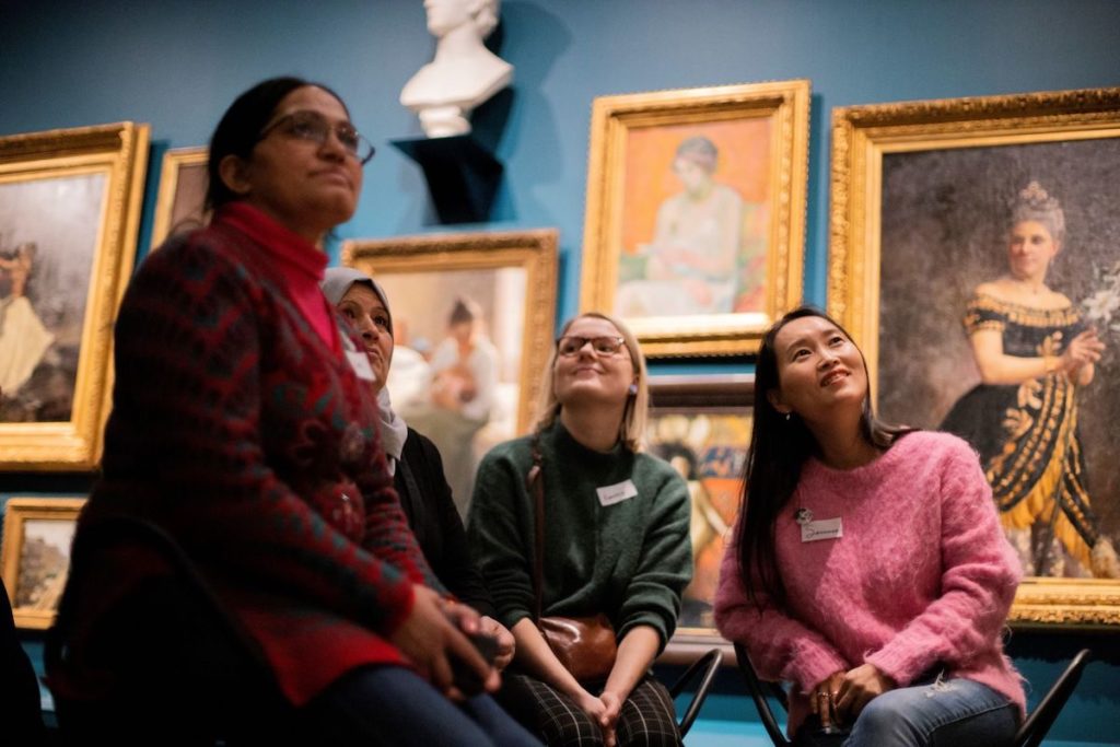 4 naista istuu museon taidenäyttelyssä