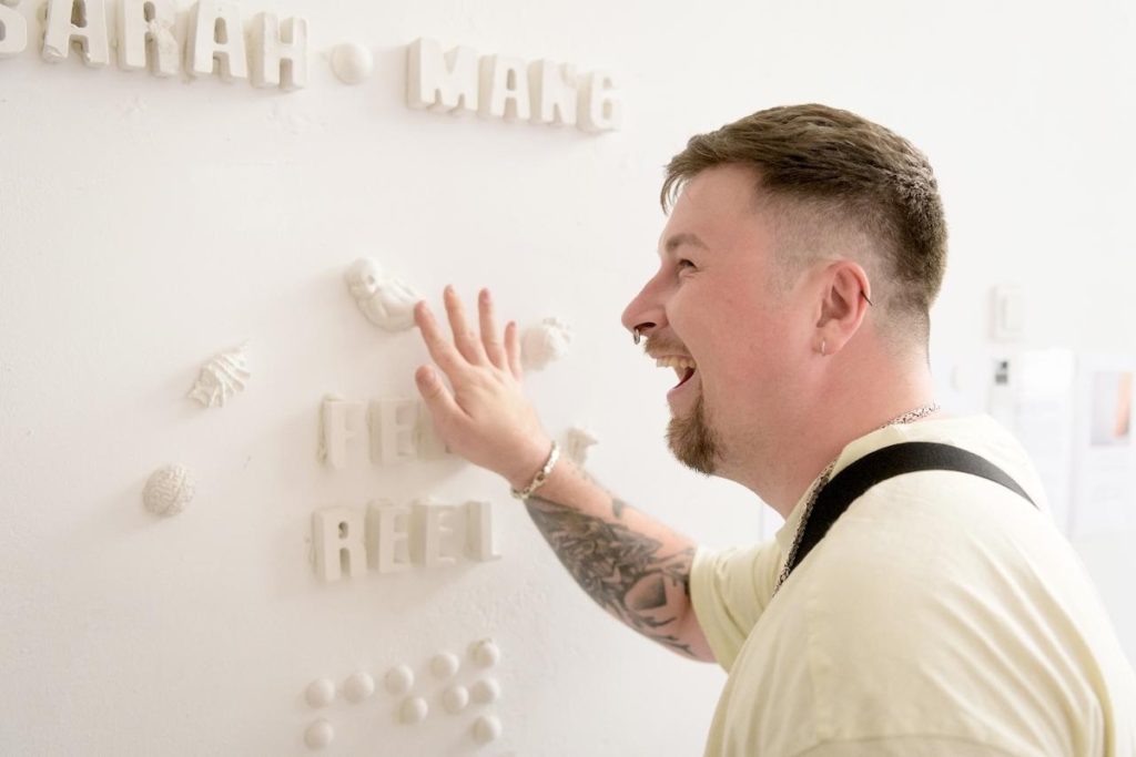 Naurava nuori mies koskettelee valkoisia reliefikuvia seinällä.